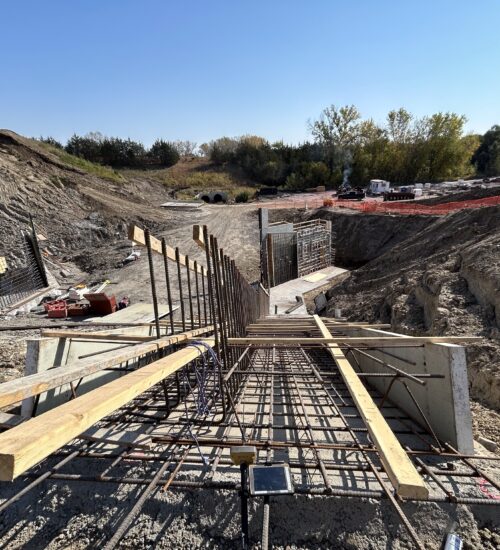Construction site with rebar, wooden supports, dirt, equipment under sky.