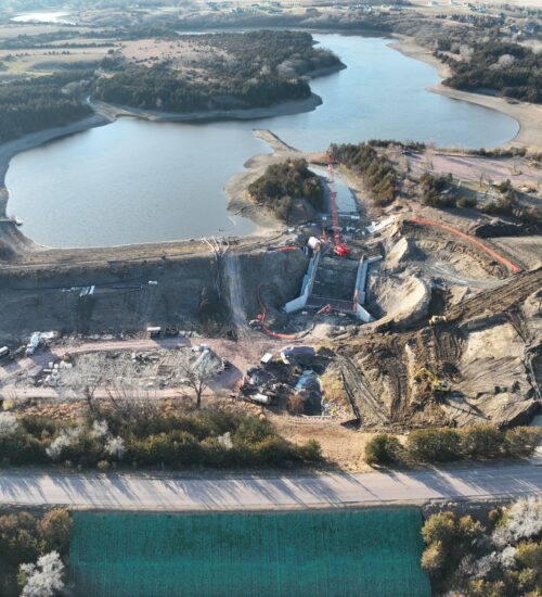 Aerial view: construction site by lake with equipment and trees.