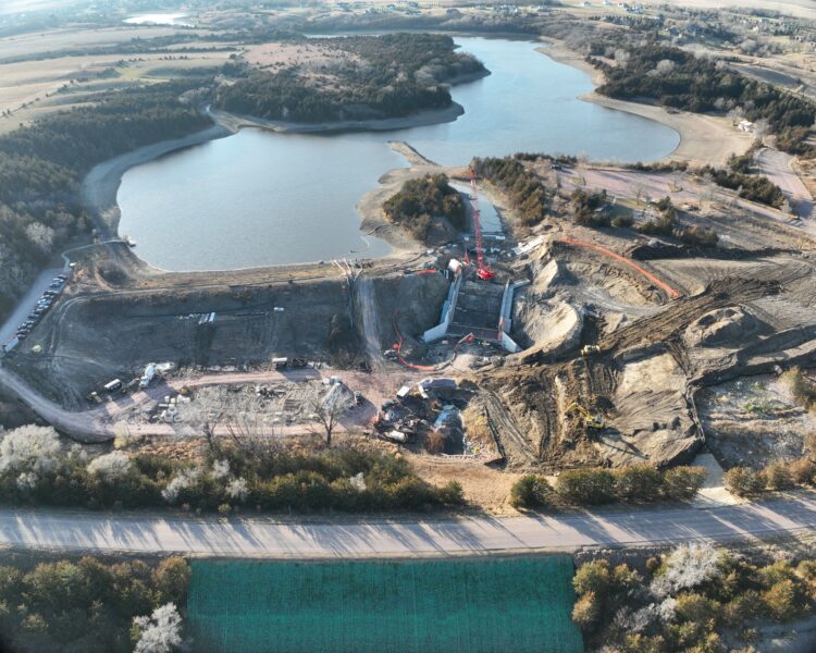 Aerial view: construction site by lake, machinery, trees, fields.