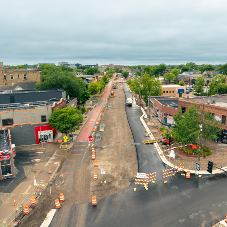 Aerial city street under construction with cones, barricades, greenery.