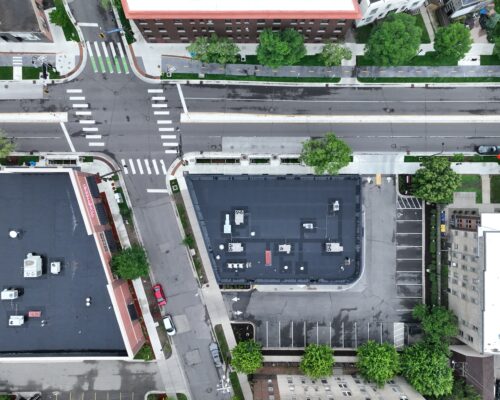 Aerial view: city intersection, crosswalks, buildings, cars, trees.