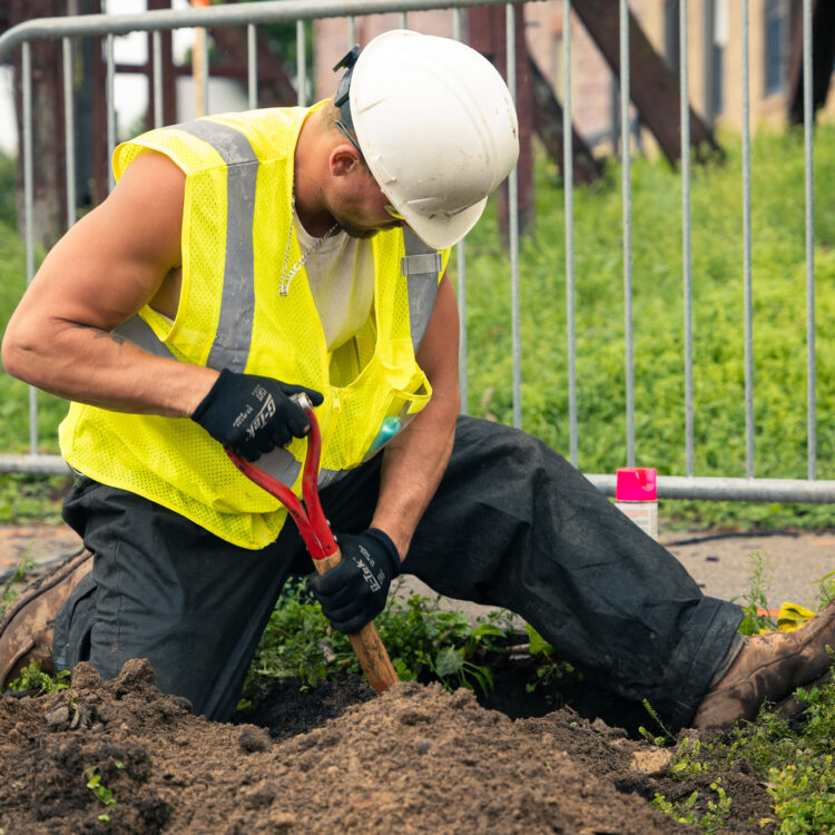 Construction worker digs soil with shovel at outdoor site.