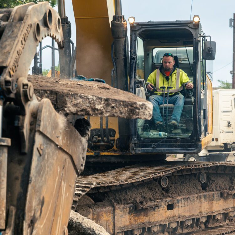Worker uses excavator to move concrete debris at site.