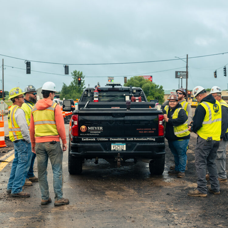 Construction workers in safety gear stand by truck at roadwork.