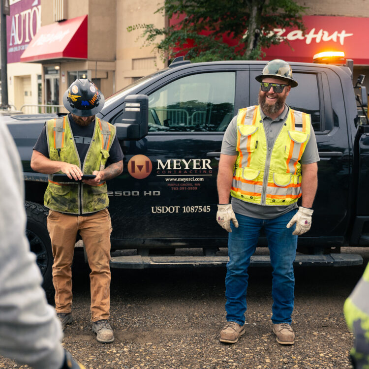 Four construction workers stand by Meyer-signed black pickup truck.