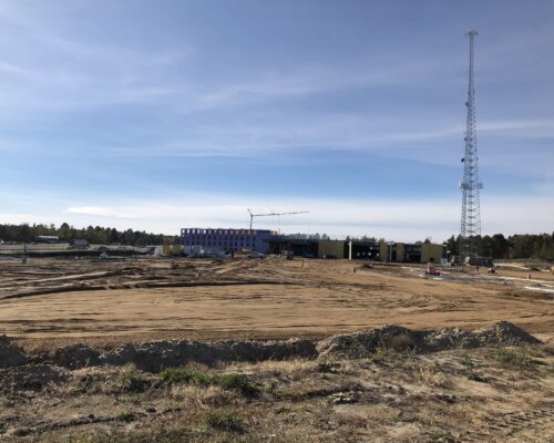 Partially built commercial building, crane, vehicles, tower, clear sky.
