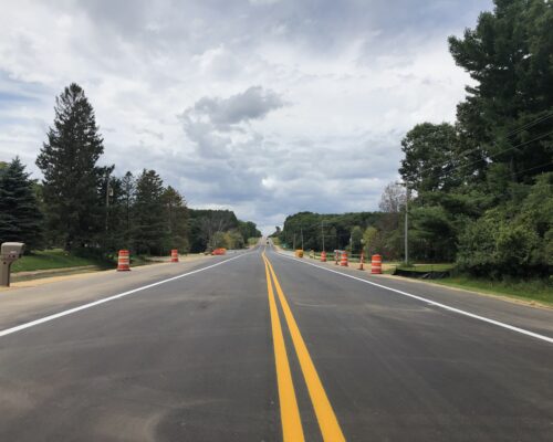 Freshly paved road with trees, barrels, and cloudy sky.