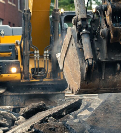 Yellow excavator moves rubble at construction site near brick building.
