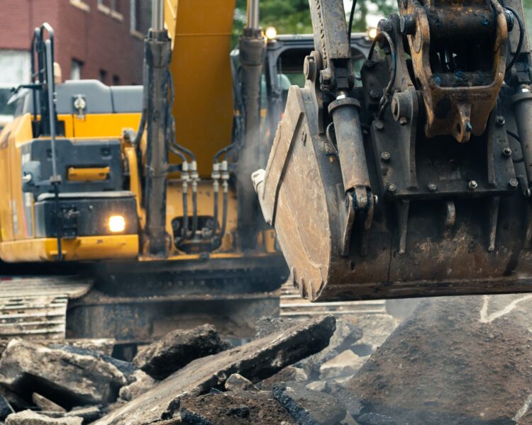 Yellow excavator moves rubble at construction site near brick building.