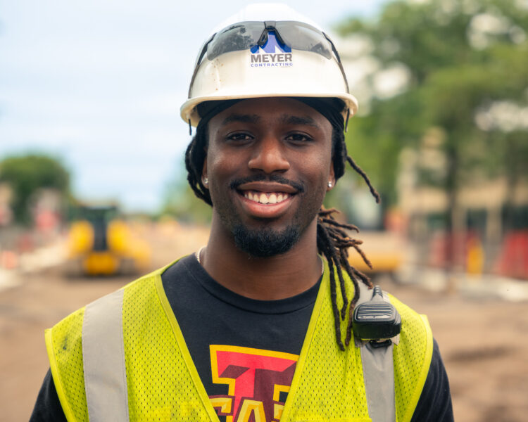 Smiling construction worker in safety gear at outdoor work site.
