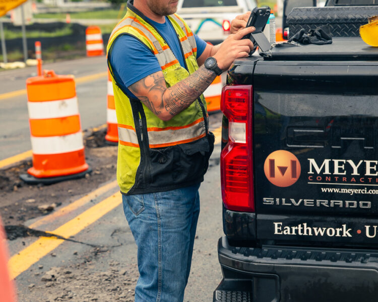 Construction worker checks phone by pickup truck at roadwork site.